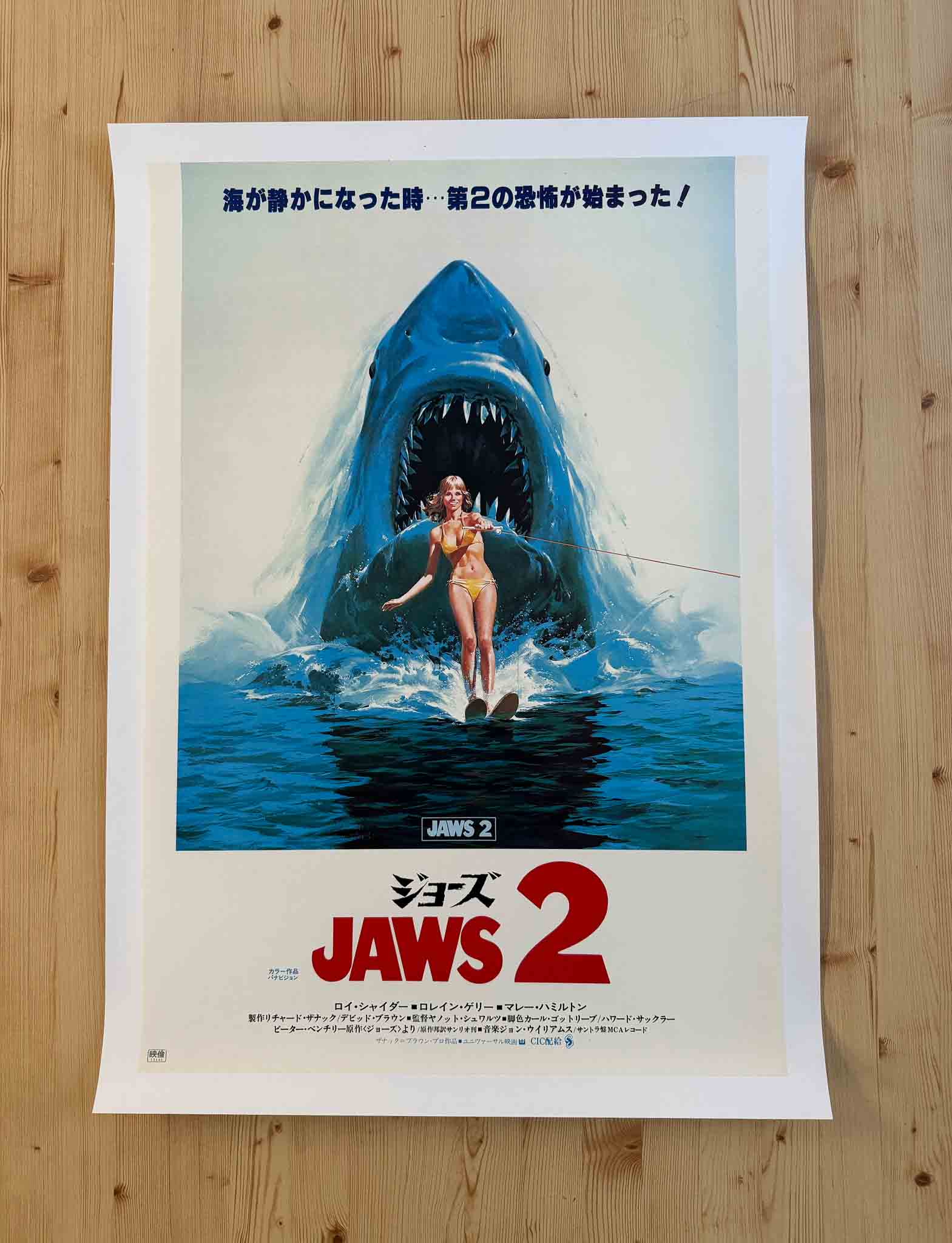 Affiche japonaise du film Jaws 2 avec un requin surgissant derrière une skieuse nautique, typographie rouge et bleue